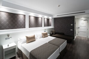A modern hotel room with a large bed, a sofa, a nightstand, and a patterned wall. - Catalonia Magdalenes (Barcelona)