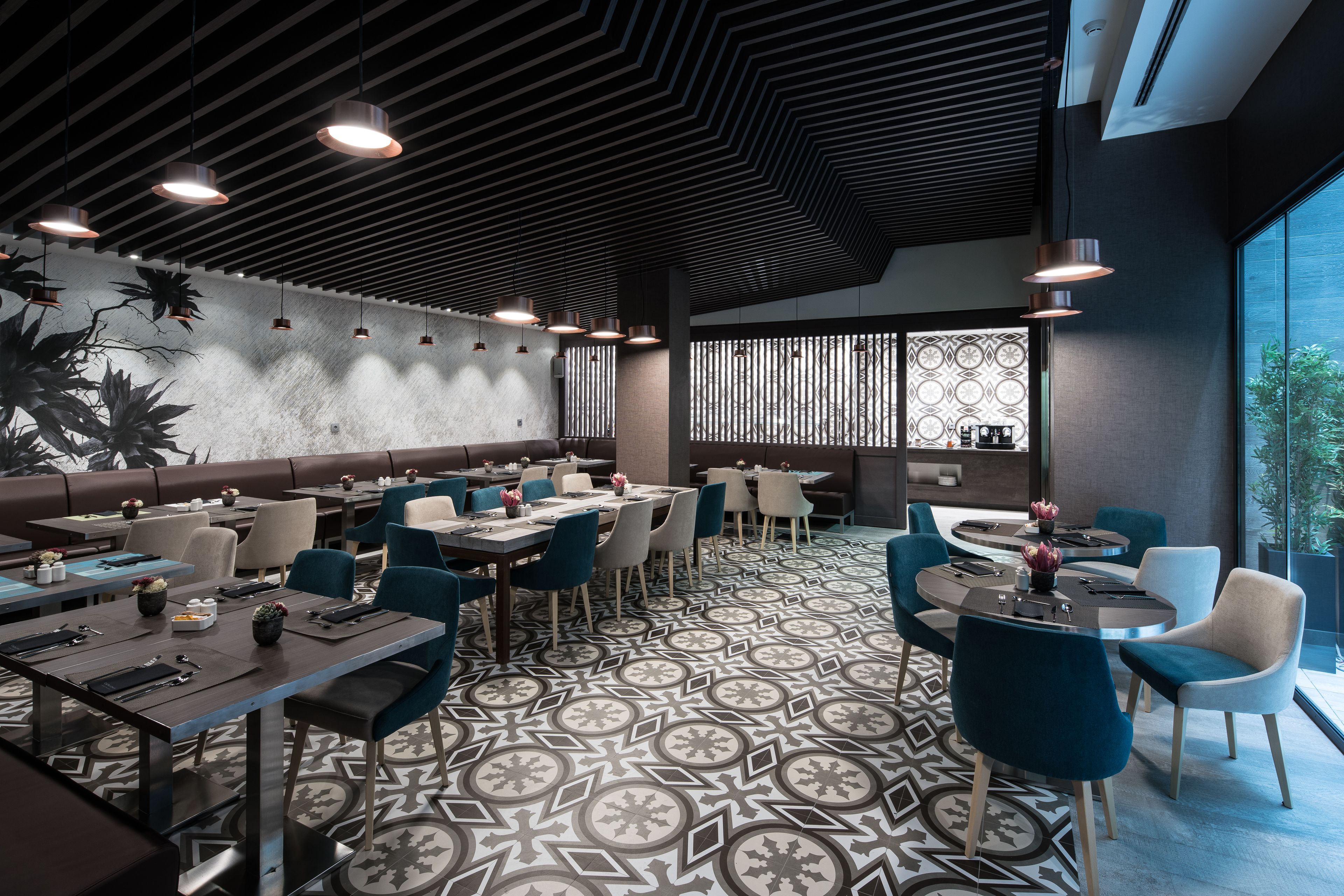 A modern restaurant with a patterned floor, multiple dining tables with chairs, and pendant lighting.