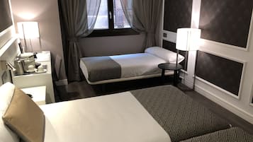 A hotel room with a large bed, a bedside table with a lamp, a small table, and a window with curtains.