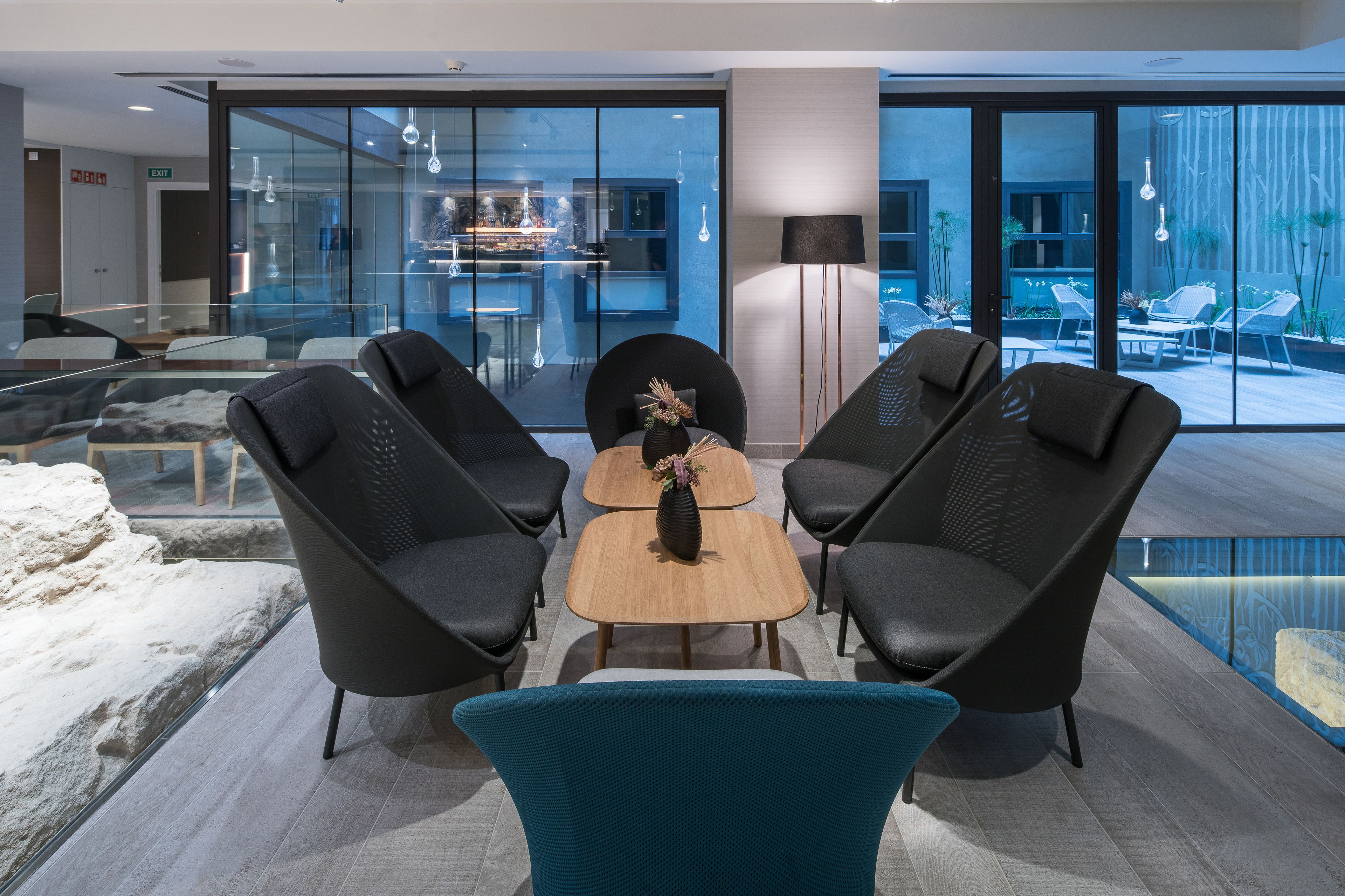 A modern indoor seating area with a glass partition, a wooden table, and black chairs.