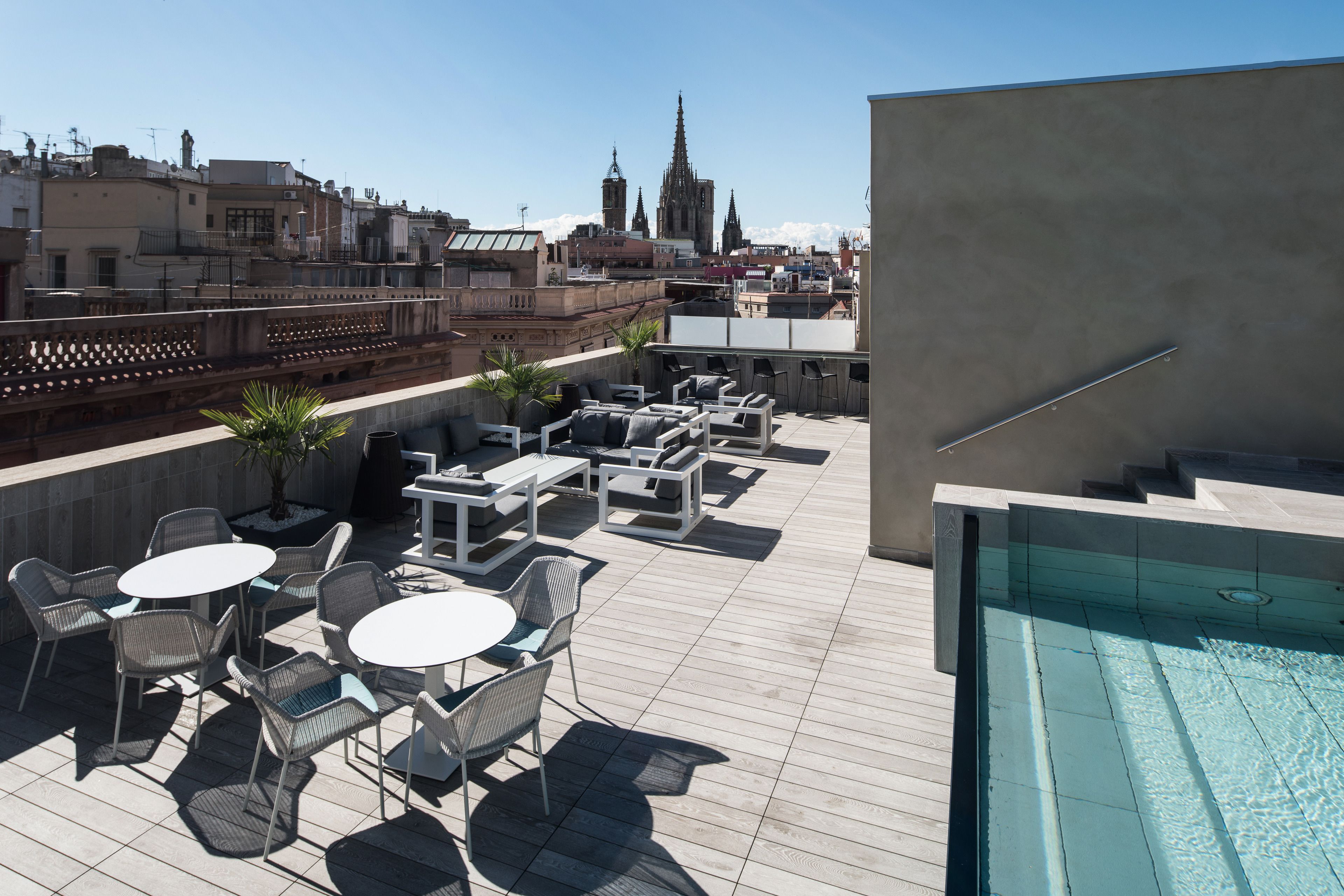 Eine Dachterrasse mit Sitzgelegenheiten im Freien, einem Schwimmbad und Blick auf einen Dom.