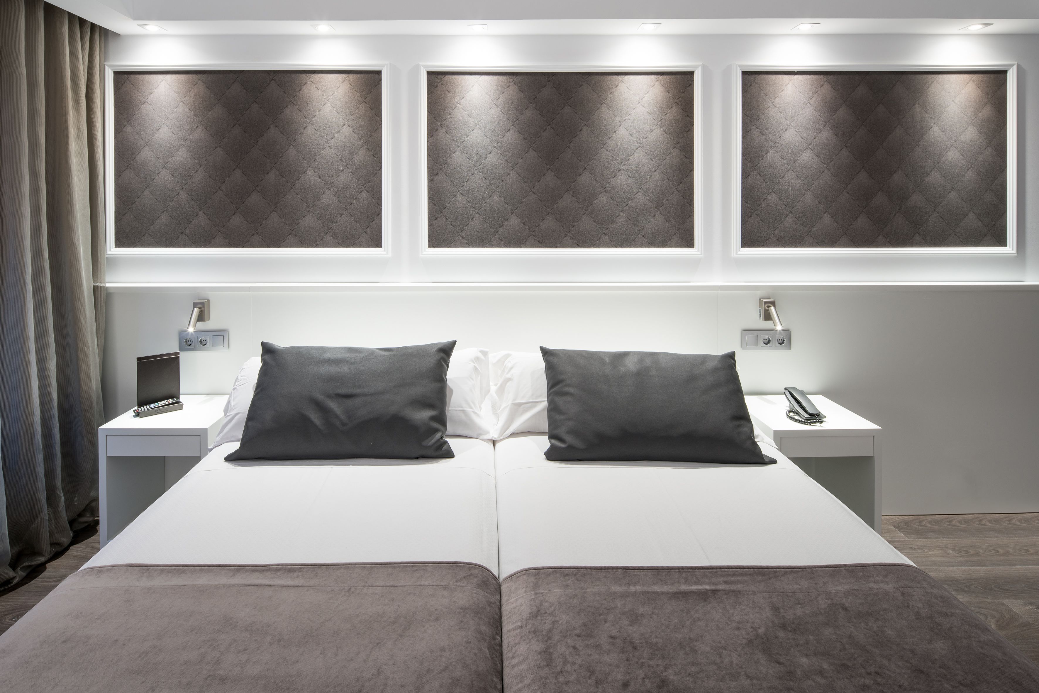 A modern hotel room with a large bed, two bedside tables, and a headboard with illuminated panels.