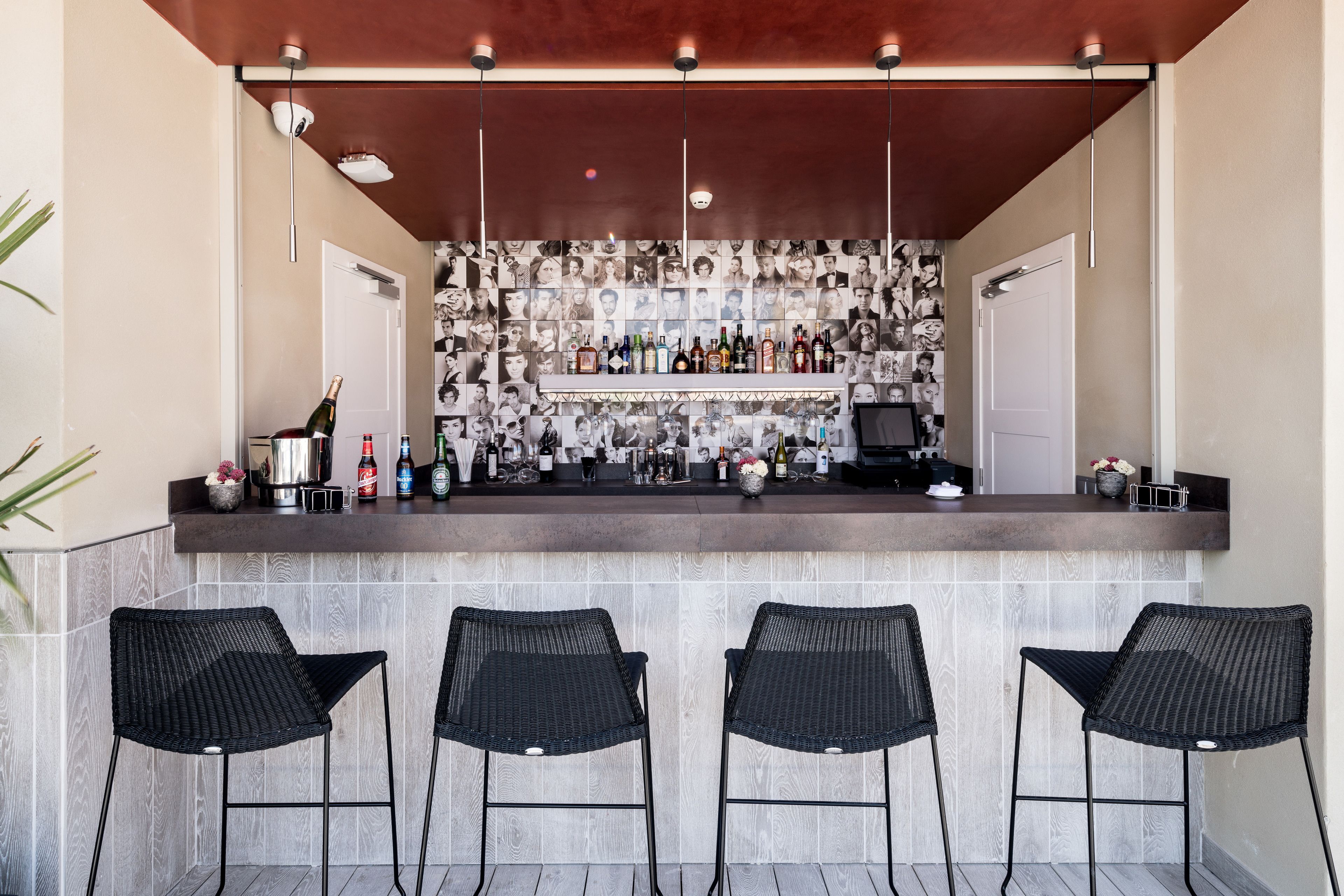 Zona de bar con salpicadero de azulejos, una variedad de botellas y taburetes de mimbre negro.
