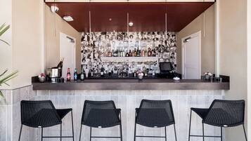 Zona de bar con salpicadero de azulejos, una variedad de botellas y taburetes de mimbre negro.