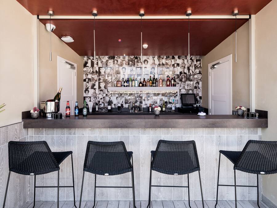 Zona de bar con salpicadero de azulejos, una variedad de botellas y taburetes de mimbre negro.