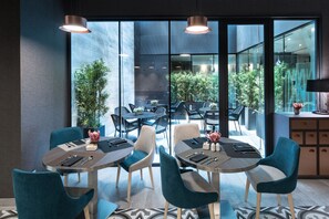 A modern dining area with round tables, teal chairs, and a view of the outdoor patio. - Catalonia Magdalenes (Barcelona)