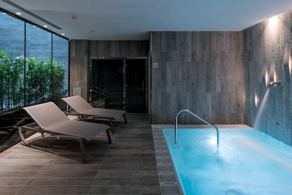 A modern spa area with a hot tub, lounge chairs, and a view of greenery through large windows. - Catalonia Magdalenes (Barcelona)