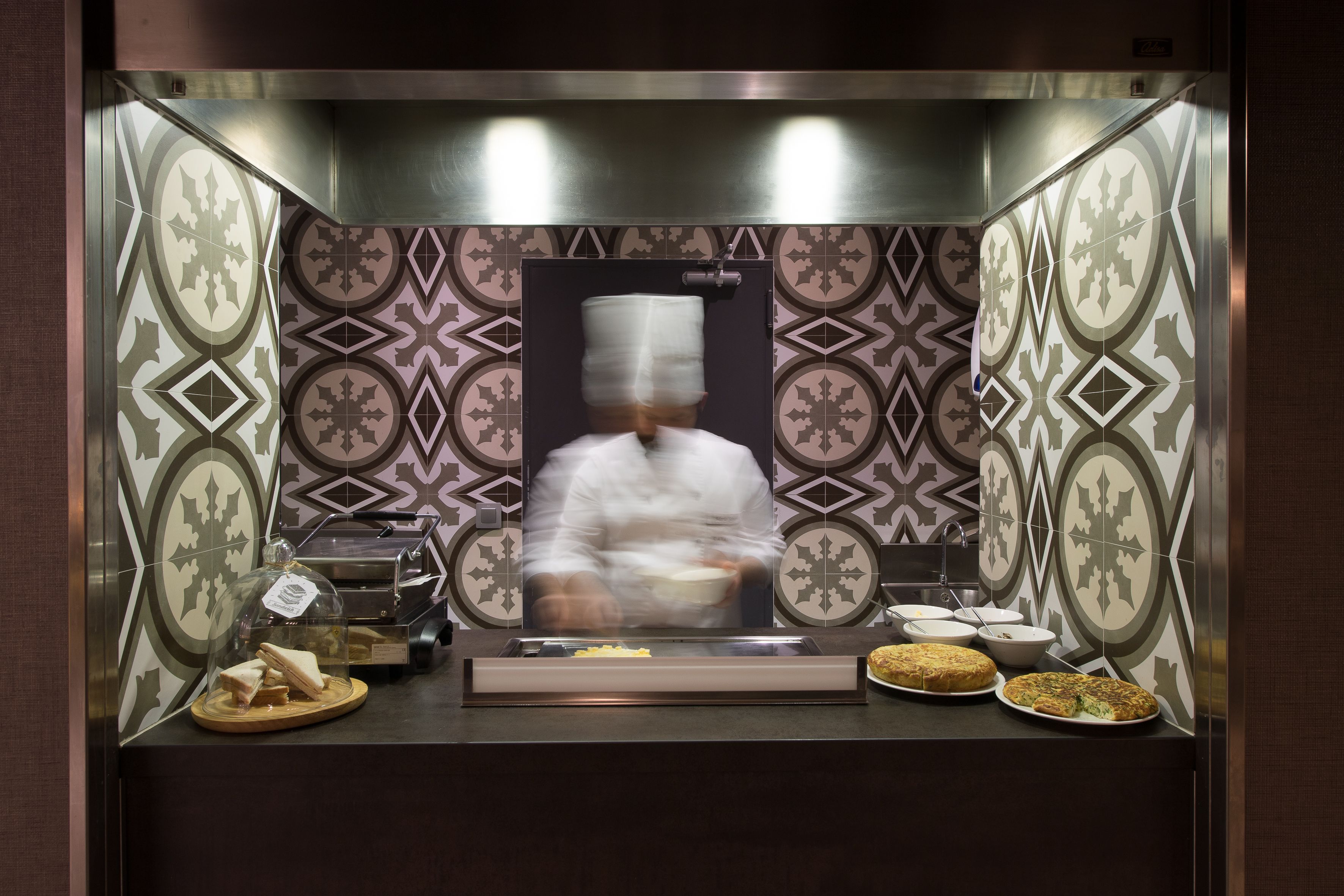 Una estación de cocina con salpicadero de azulejos, un extractor de humos y varios alimentos expuestos sobre la encimera.