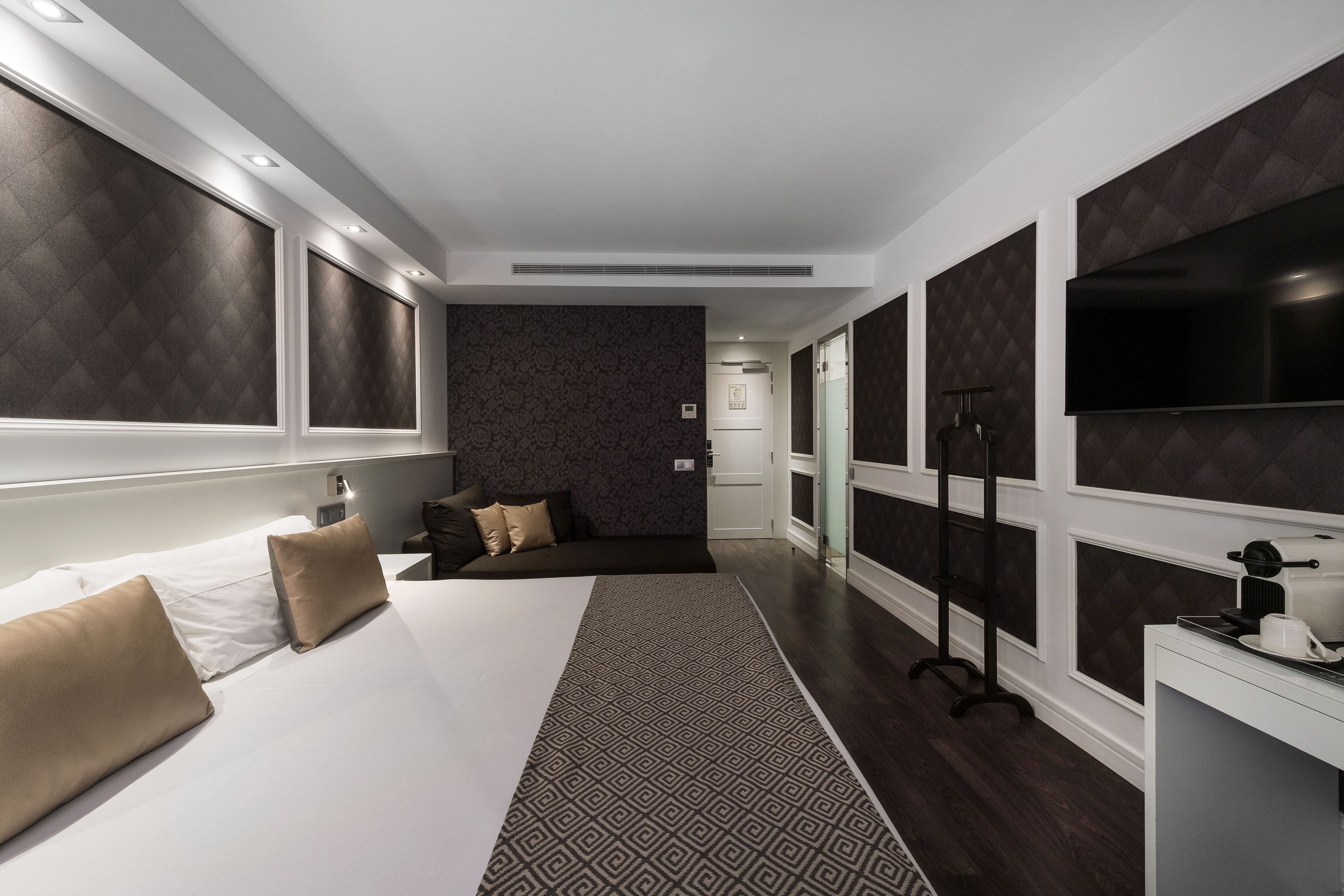Une chambre d’hôtel moderne dotée d’un grand lit, d’un bureau avec une machine à café et d’un téléviseur fixé au mur.