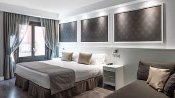 A modern hotel room with a large bed, bedside tables, and a sofa.