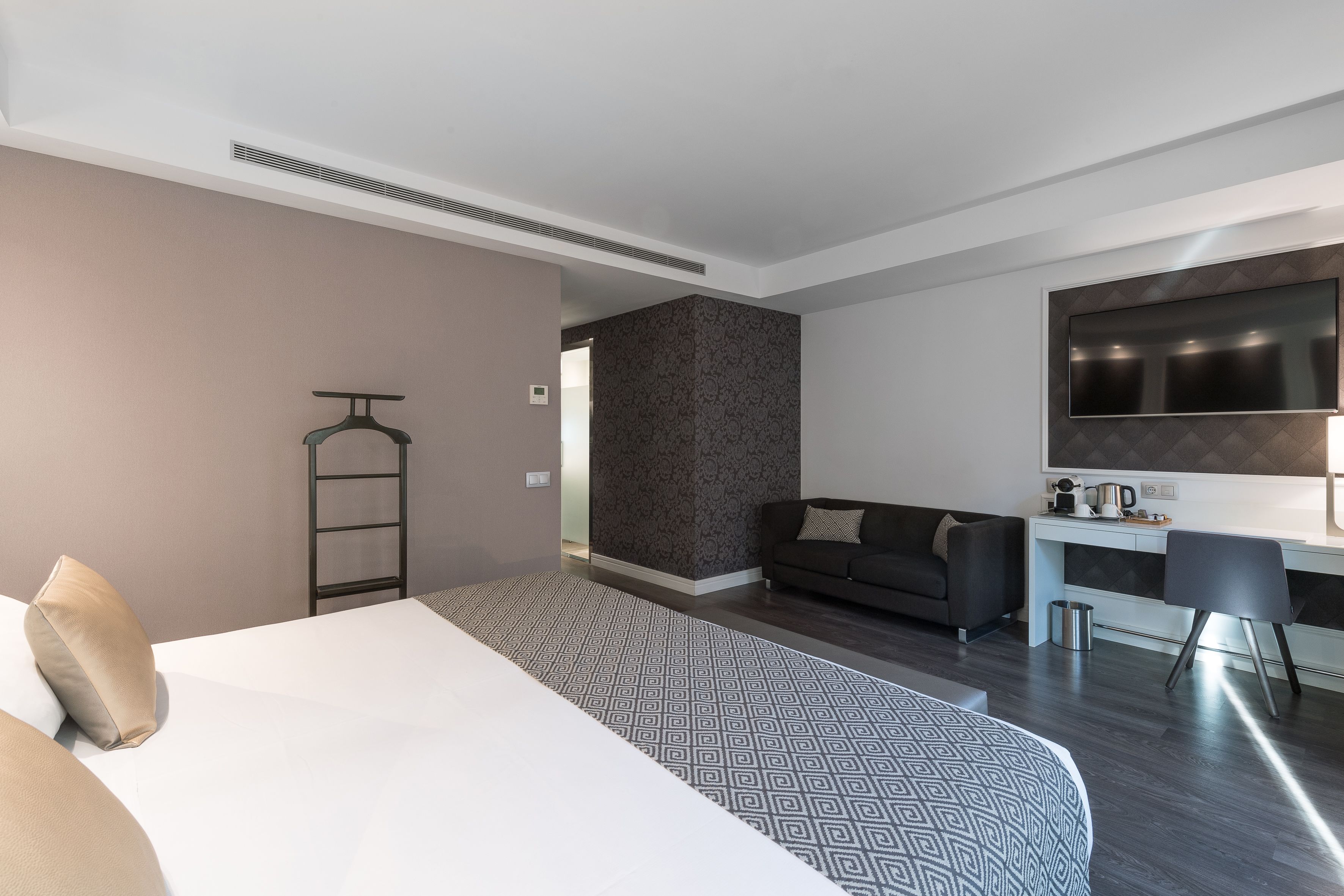 Moderni hotellihuone, jossa on sänky, työpöytä, sohva ja televisio.