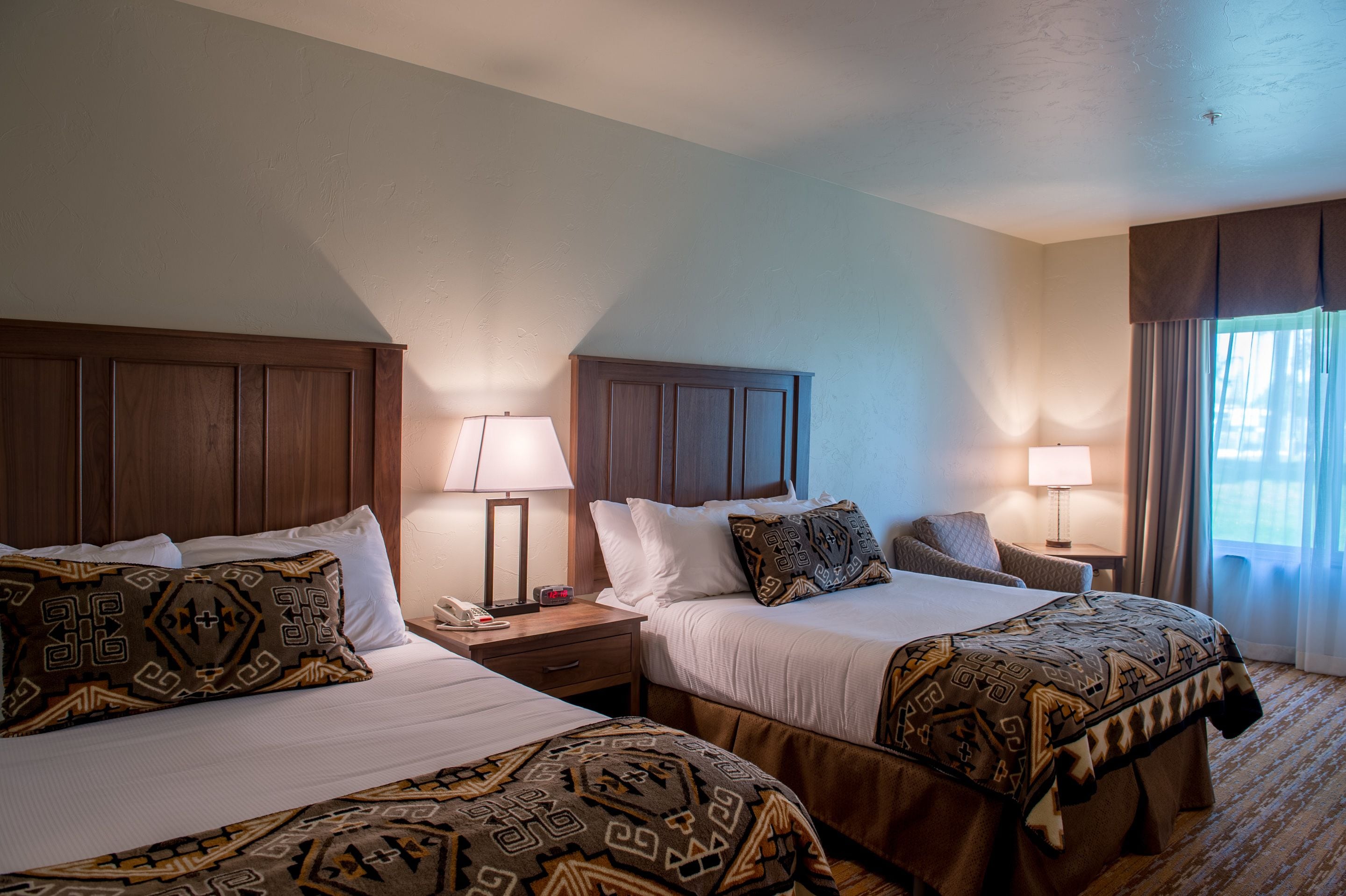 Une chambre d’hôtel avec deux lits, chacun agrémenté de draps à motifs, de têtes de lit en bois, de tables de chevet avec des lampes et d’une fenêtre avec des rideaux.