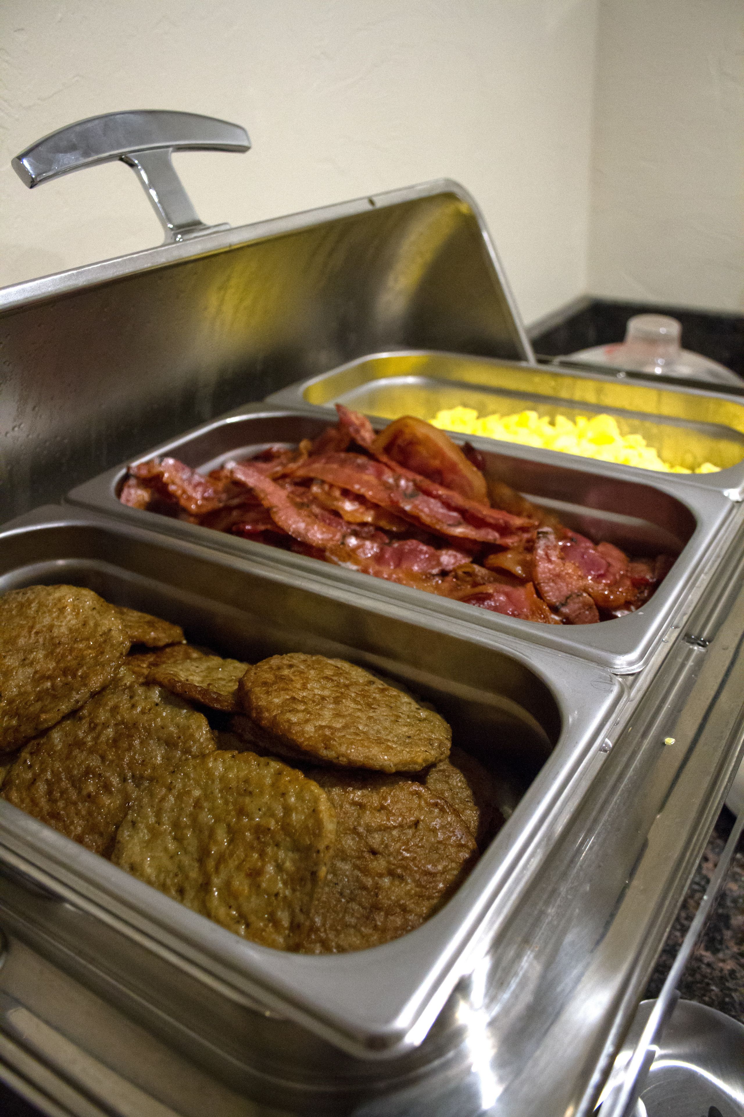 A buffet with various food items including bacon, eggs, and meatballs.