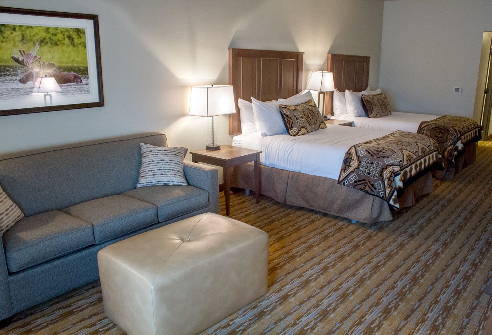 A hotel room with a bed, a sofa, a nightstand, a lamp, and a framed picture on the wall.