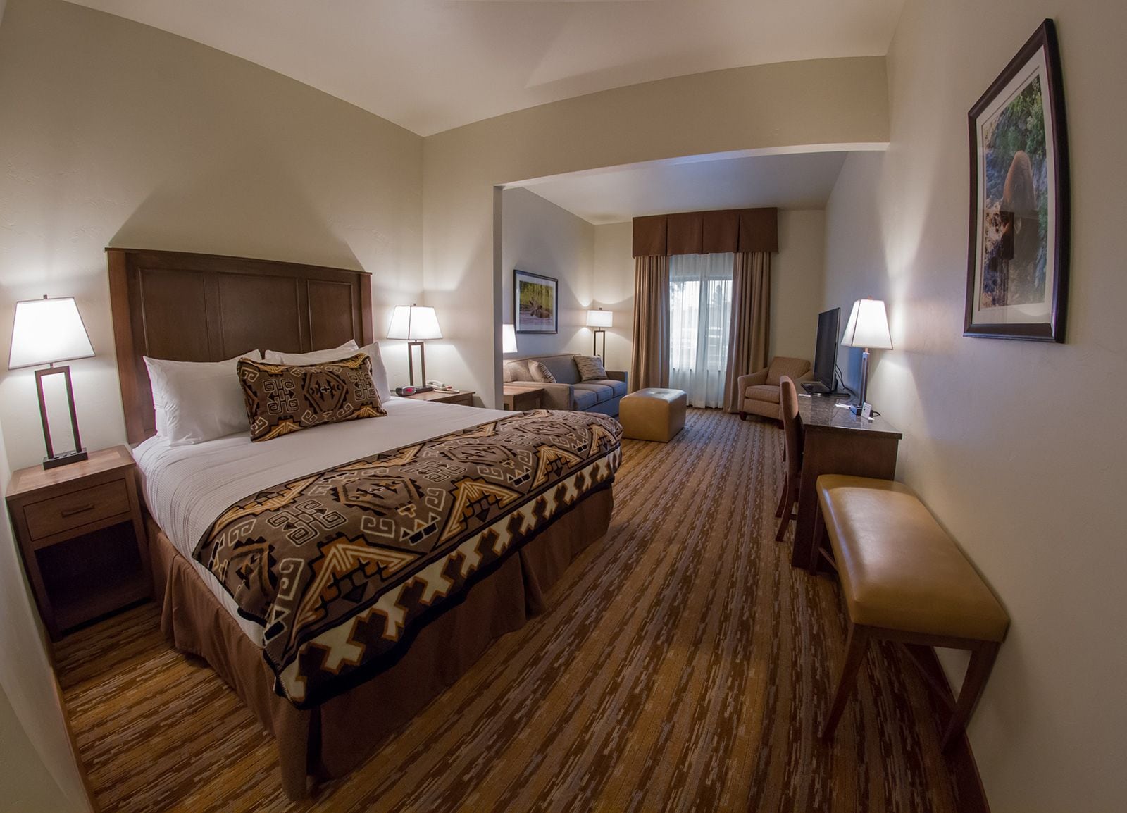 A hotel room with a large bed, two bedside tables, a desk, a chair, and a TV.