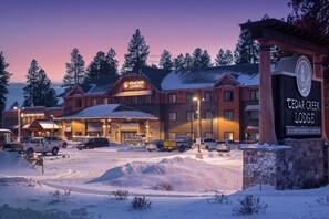 A lodge with a prominent sign, multiple parking spaces, and a snowy landscape. - Cedar Creek Lodge and Conference Center (Columbia Falls)