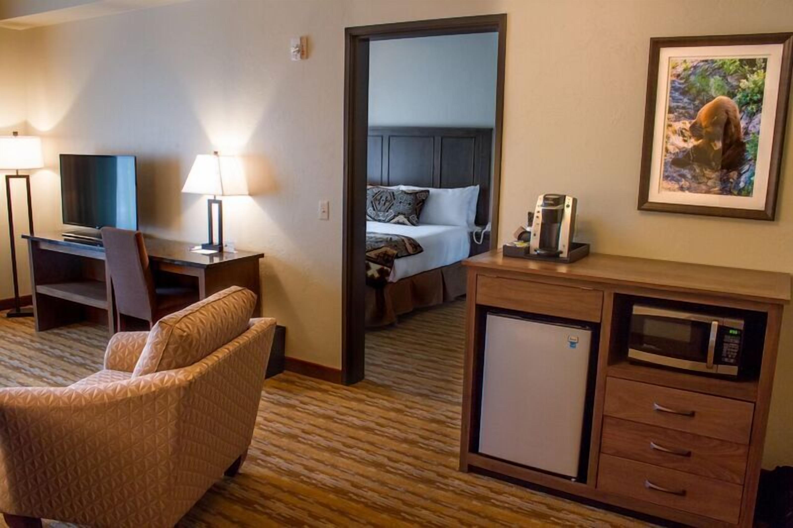 A hotel room with a bed, a desk with a TV, a chair, a microwave, and a small refrigerator.