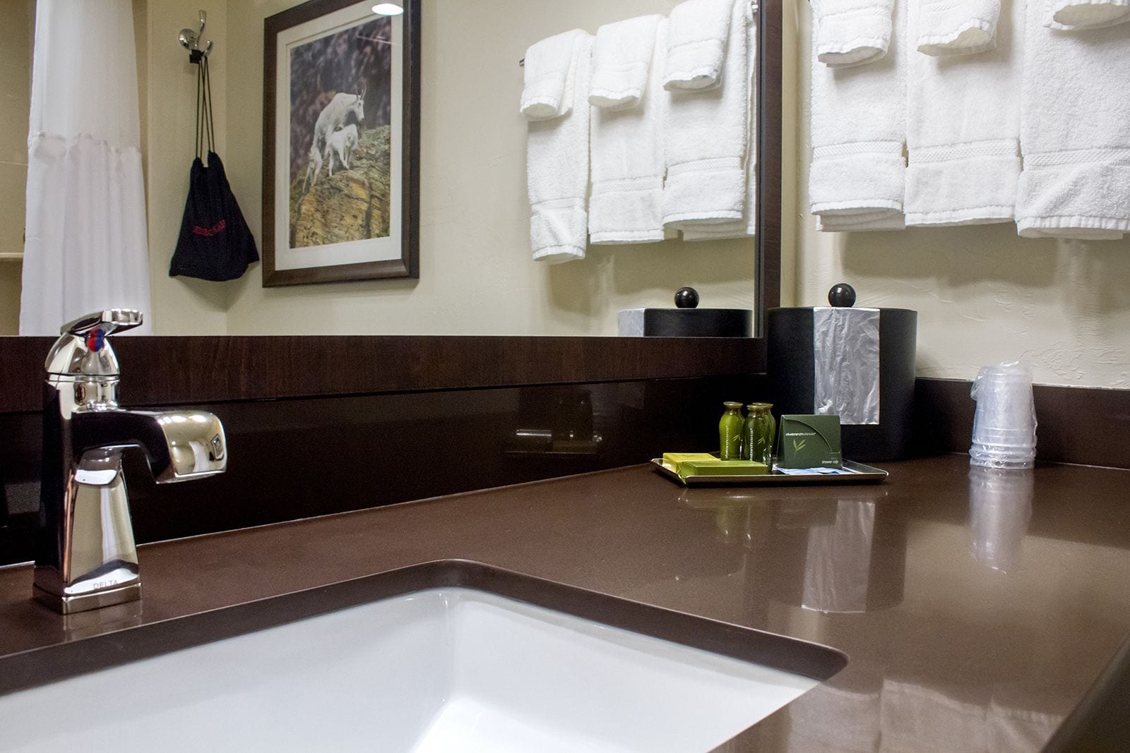 Un baño de hotel con lavamanos, espejo y toallero con toallas blancas.