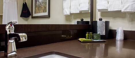 Un baño de hotel con lavamanos, espejo y toallero con toallas blancas.