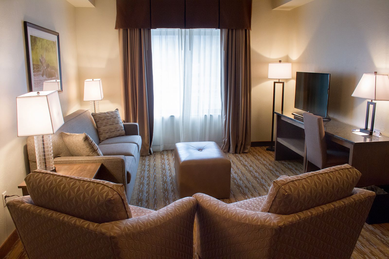Une chambre d’hôtel comprenant un canapé, deux fauteuils, une table basse, un téléviseur et un bureau avec des lampes.