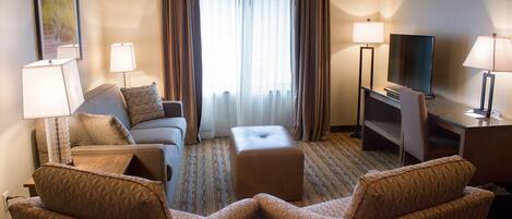 Une chambre d’hôtel comprenant un canapé, deux fauteuils, une table basse, un téléviseur et un bureau avec des lampes.