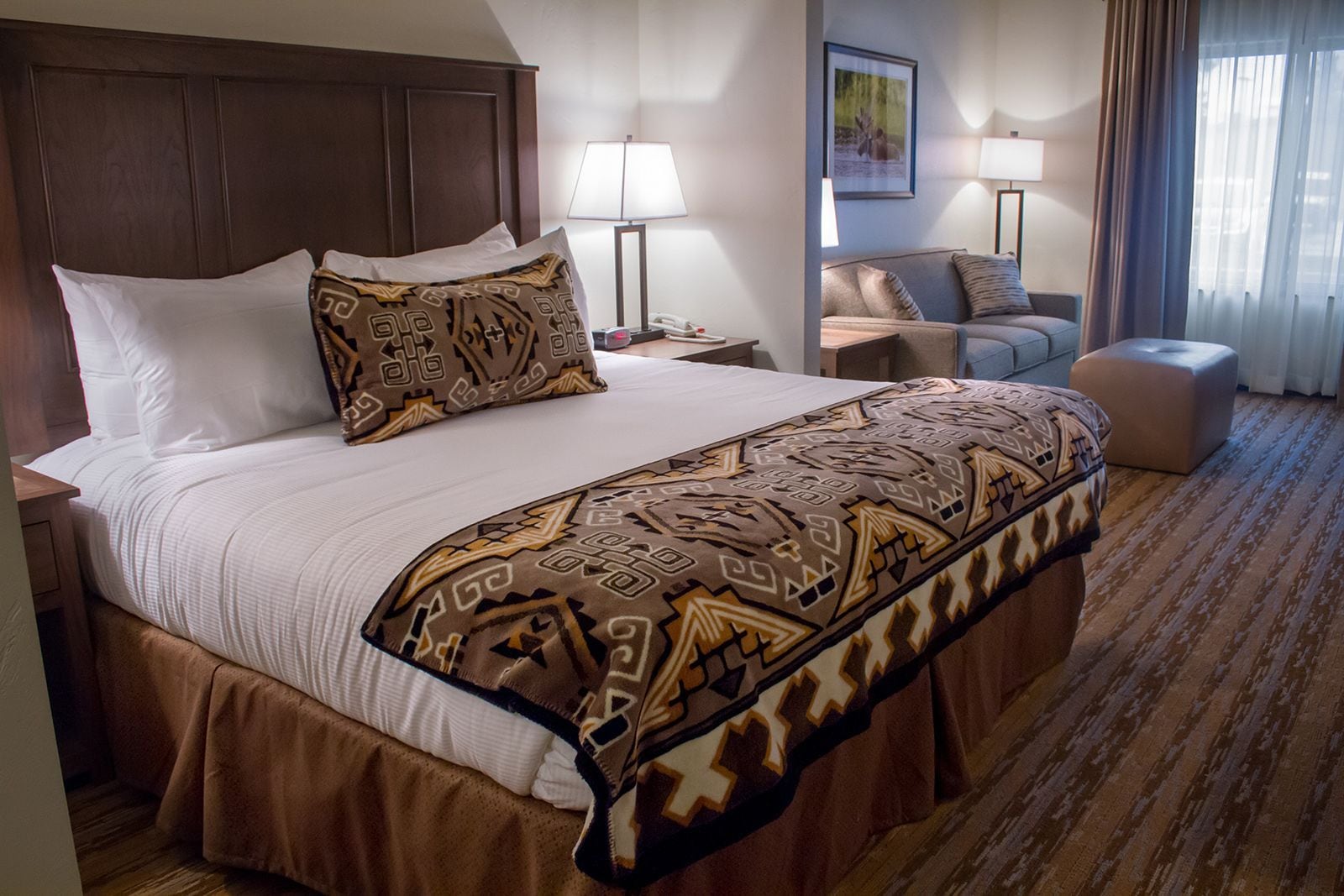 A hotel room with a large bed, two bedside tables, a sofa, a chair, and a small ottoman.