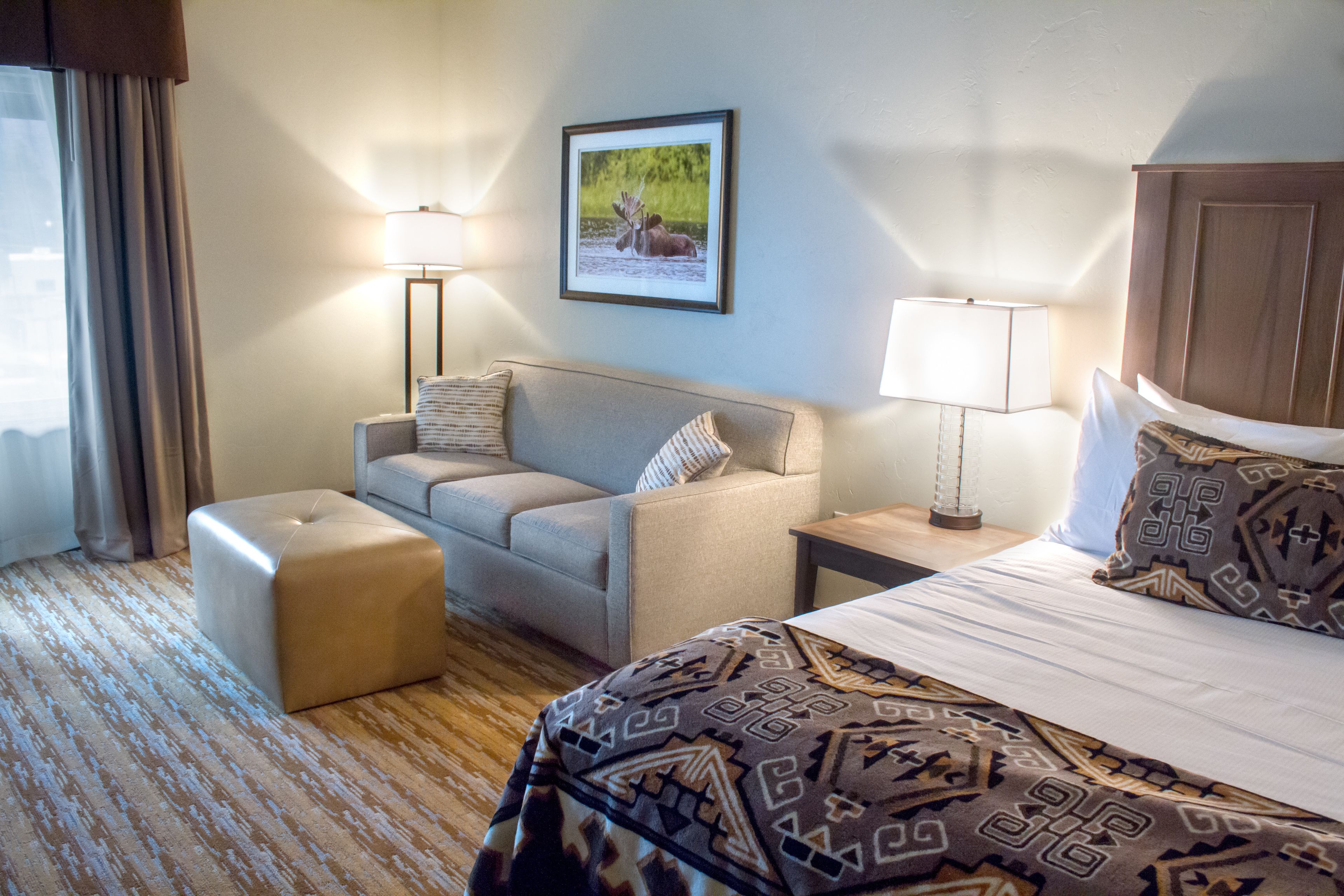 Habitación de hotel con una cama, un sofá, una mesita, una lámpara y un cuadro en la pared.