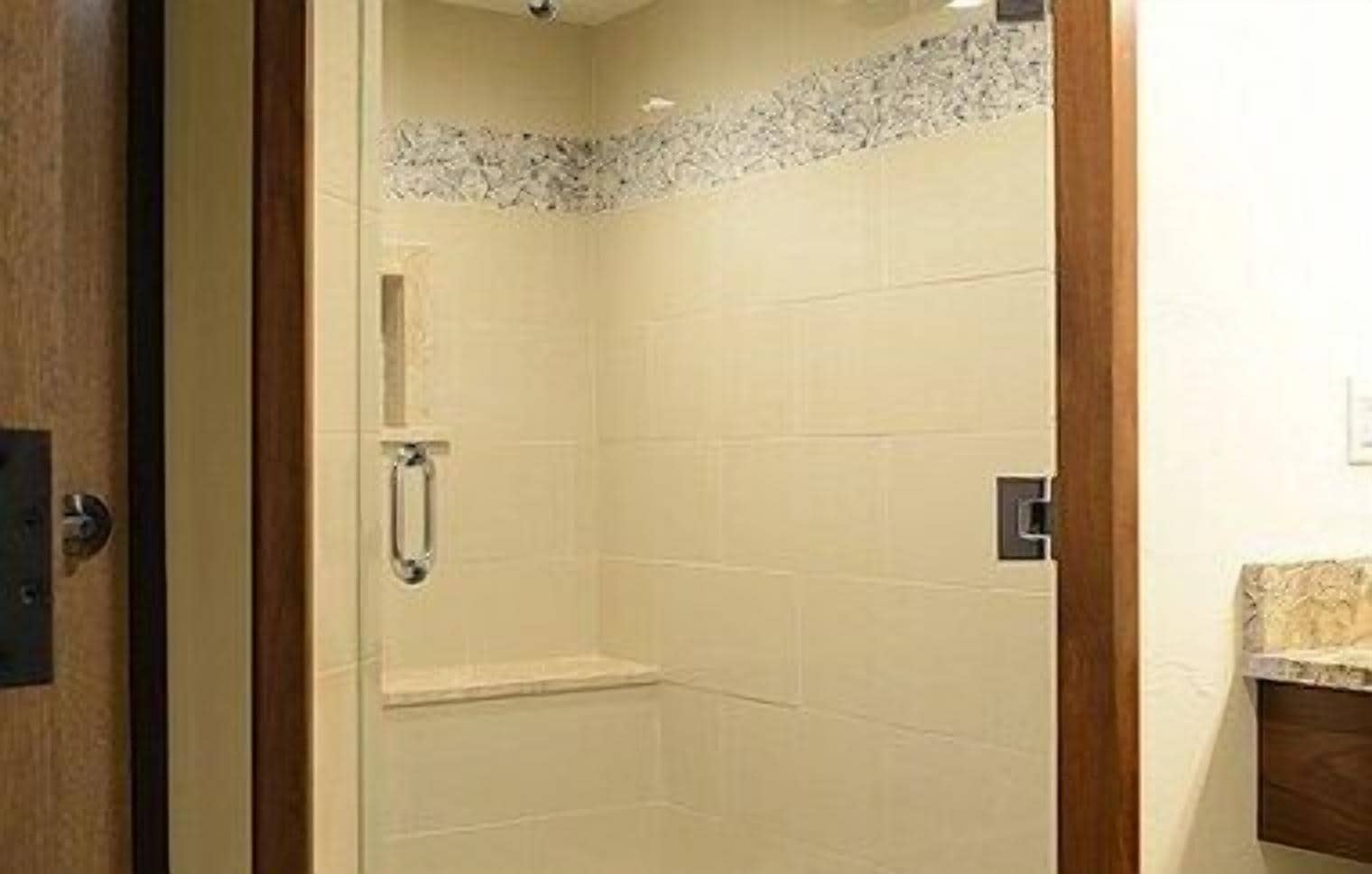 A shower with a glass door, a wooden frame, and a tiled wall.