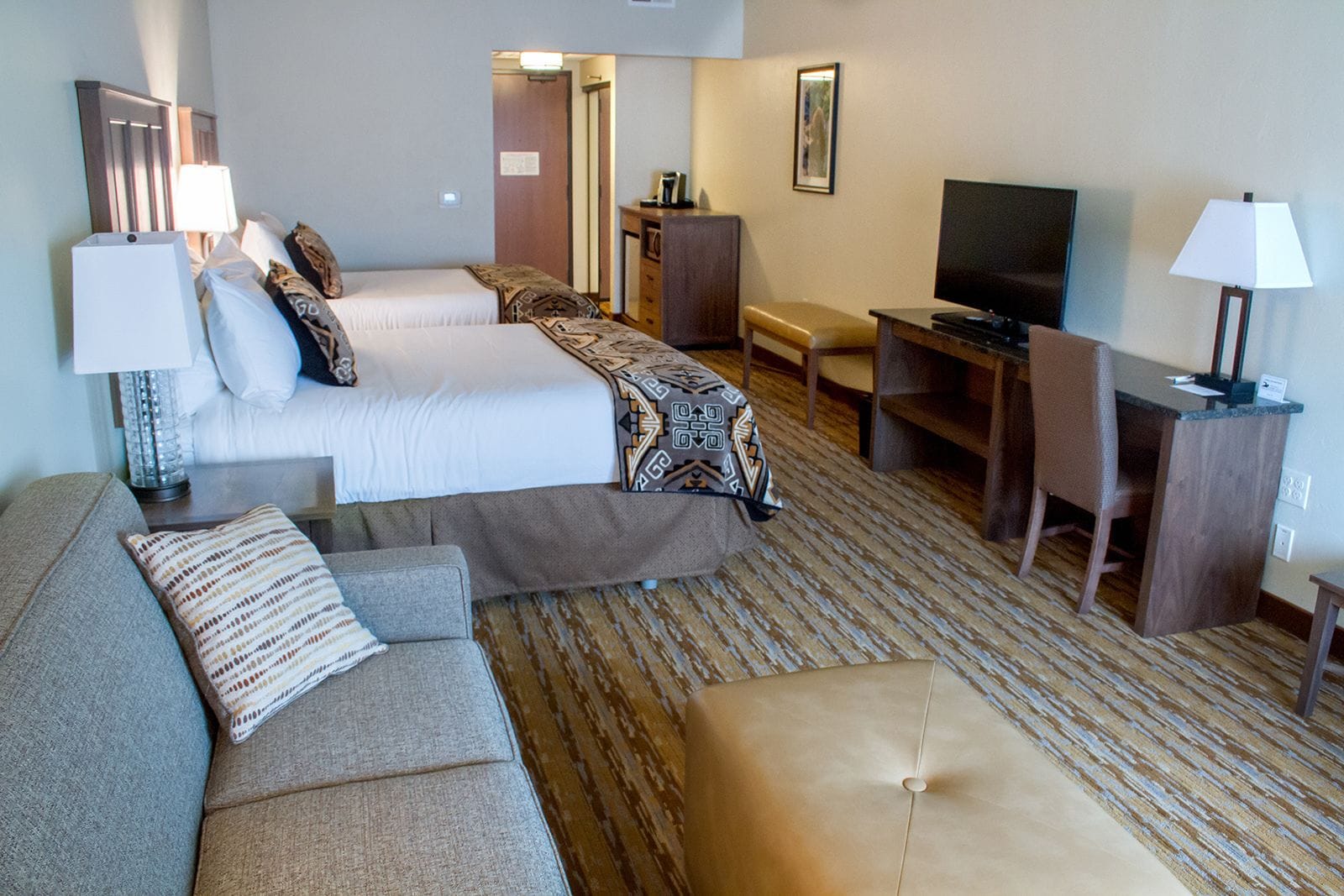 Una habitación de hotel con cama, sofá, escritorio, televisor y espejo.