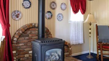 Um quarto com lareira de tijolos, uma cadeira de madeira, um abajur e uma cortina vermelha.