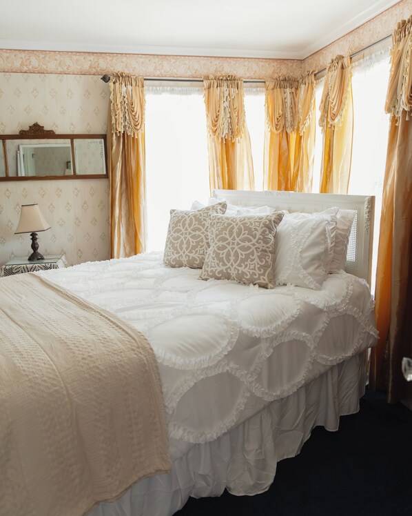 A neatly made bed with white linens and decorative pillows, a bedside table with a lamp, and a mirror on the wall. - Julian Gold Rush Hotel (Julian)