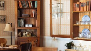 A traditional dining room with a wooden table, chairs, a bookshelf, and a cabinet with china and glassware. - Julian Gold Rush Hotel (Julian)
