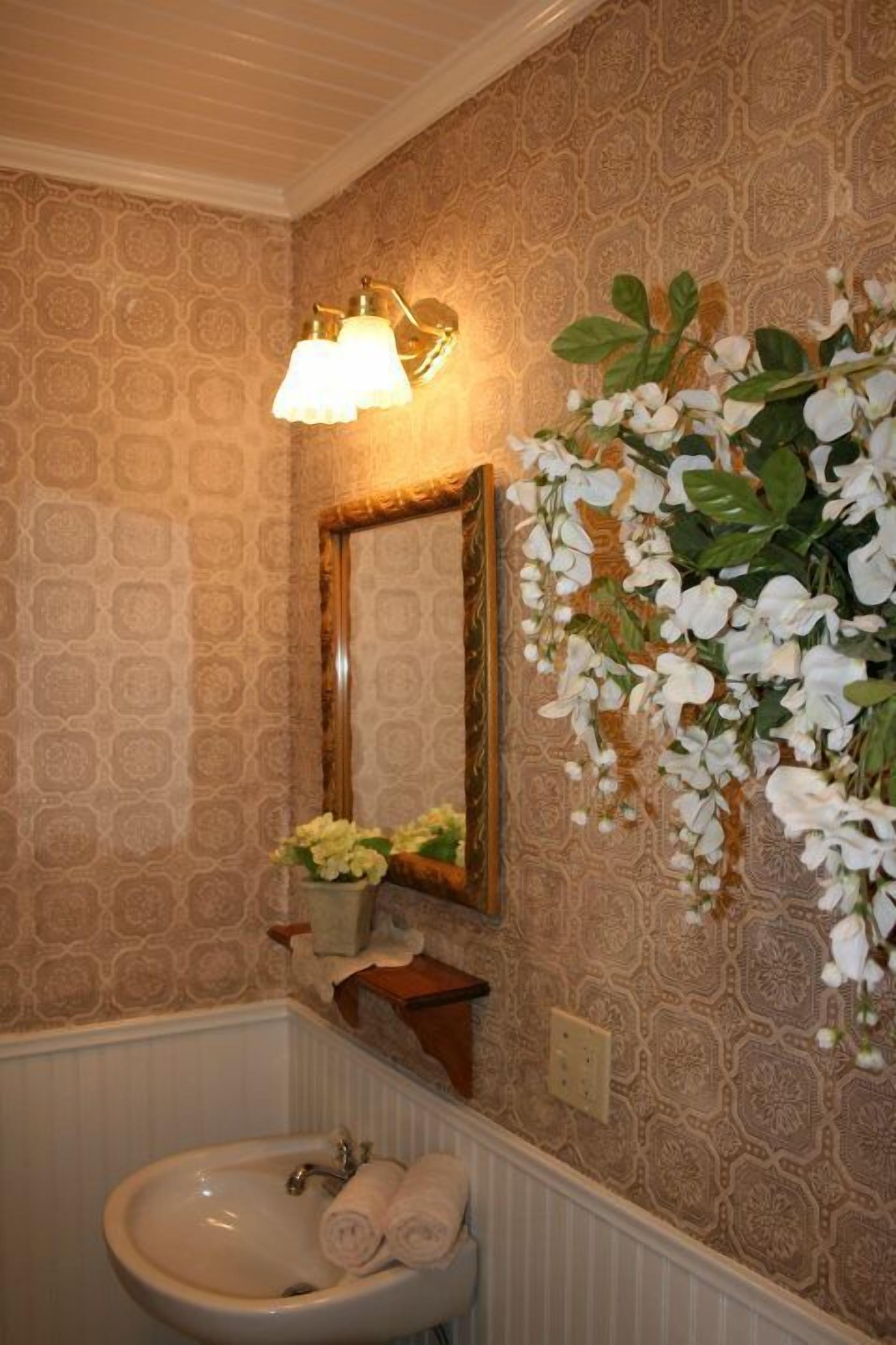 A bathroom with a sink, mirror, and decorative flowers.