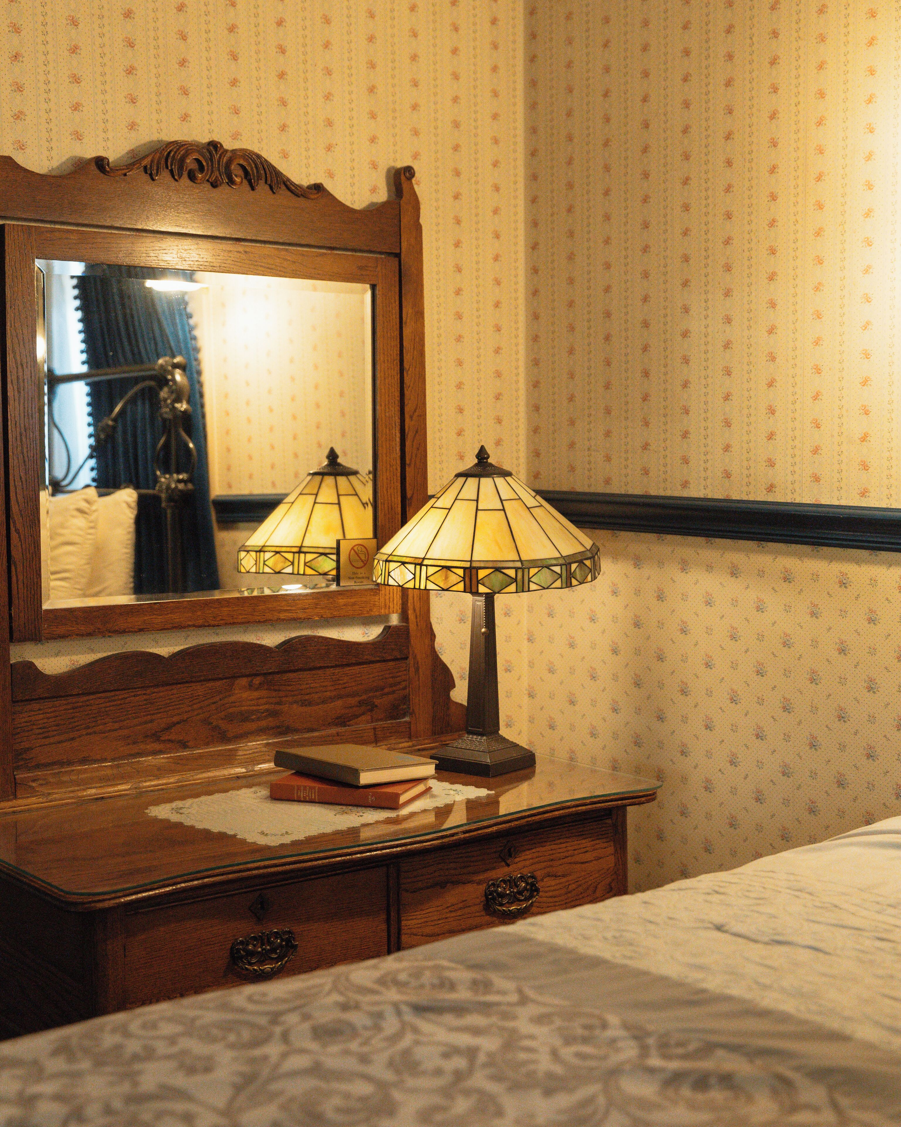 Un comò in legno con due lampade, uno specchio e un letto con carta da parati a motivi floreali.