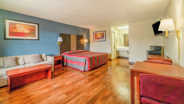 A hotel room with a wooden floor, a sofa, a bed with a colorful quilt, a desk, a chair, a TV, and a lamp. - Executive Inn By OYO Mineral Wells US-180 (Mineral Wells)