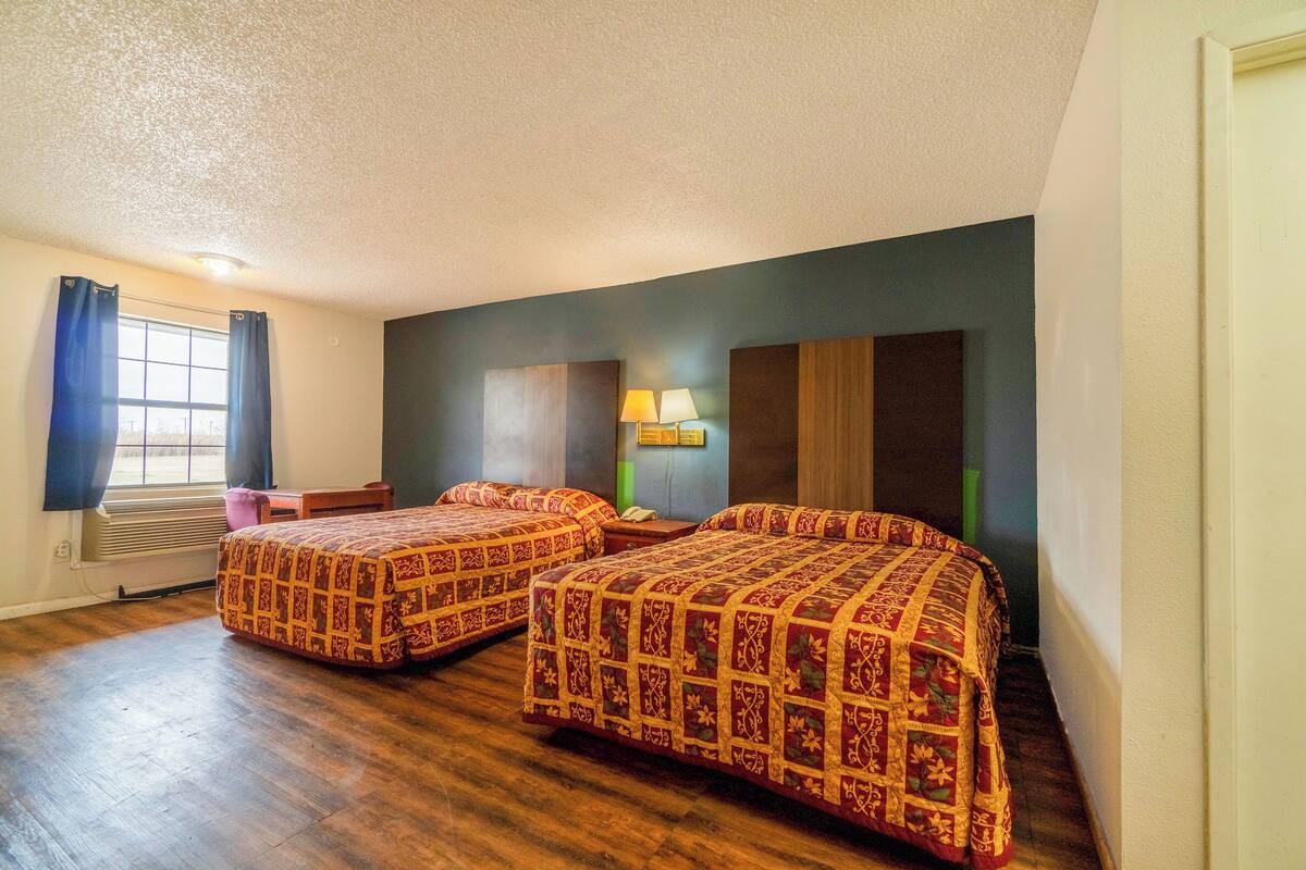 Ein Hotelzimmer mit zwei Betten, einem Fenster mit Vorhängen, einem Schreibtisch und einer Lampe.