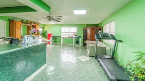 A spacious room with a green wall, a reception desk, a treadmill, a sofa, and a ceiling fan. - Executive Inn By OYO Mineral Wells US-180 (Mineral Wells)