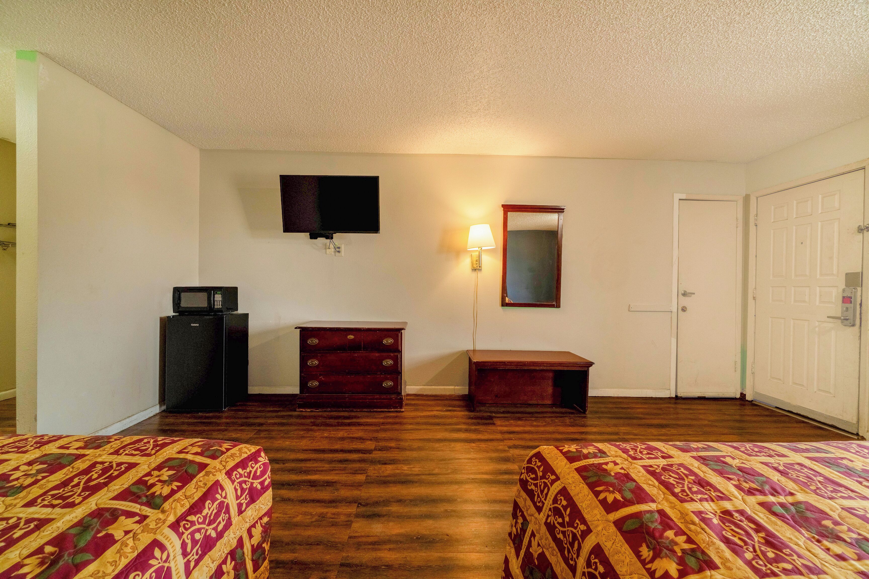 A hotel room with two beds, a TV, a dresser, a mirror, and a door.