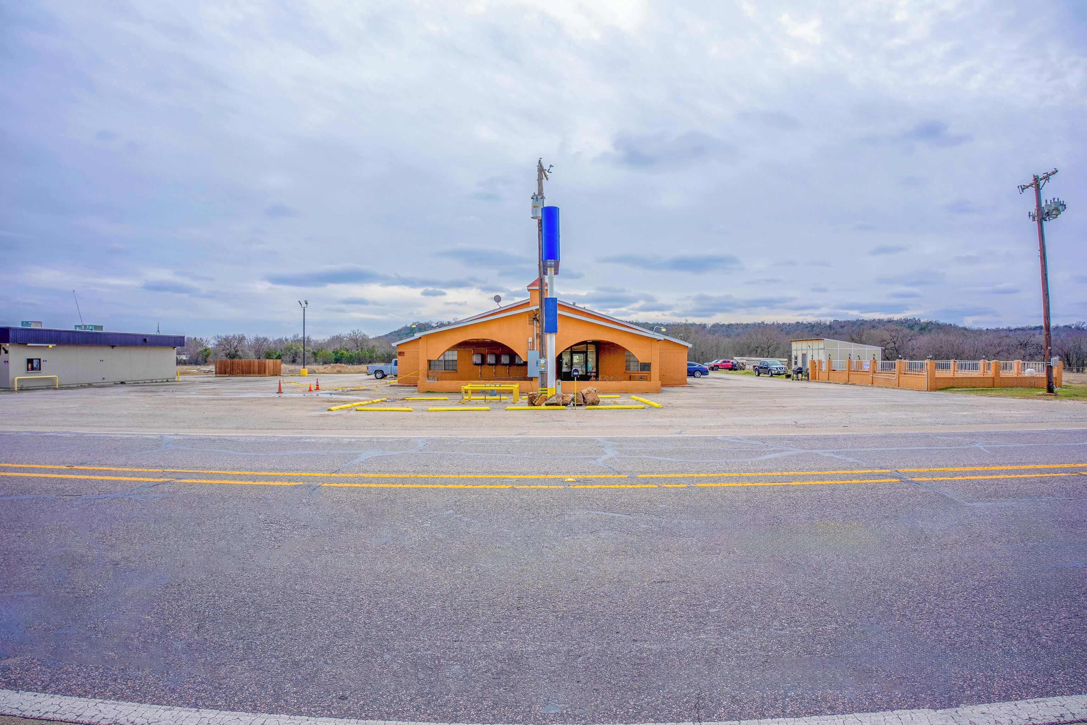 A large parking lot with a building that has a yellow roof and a blue pole in the center.
