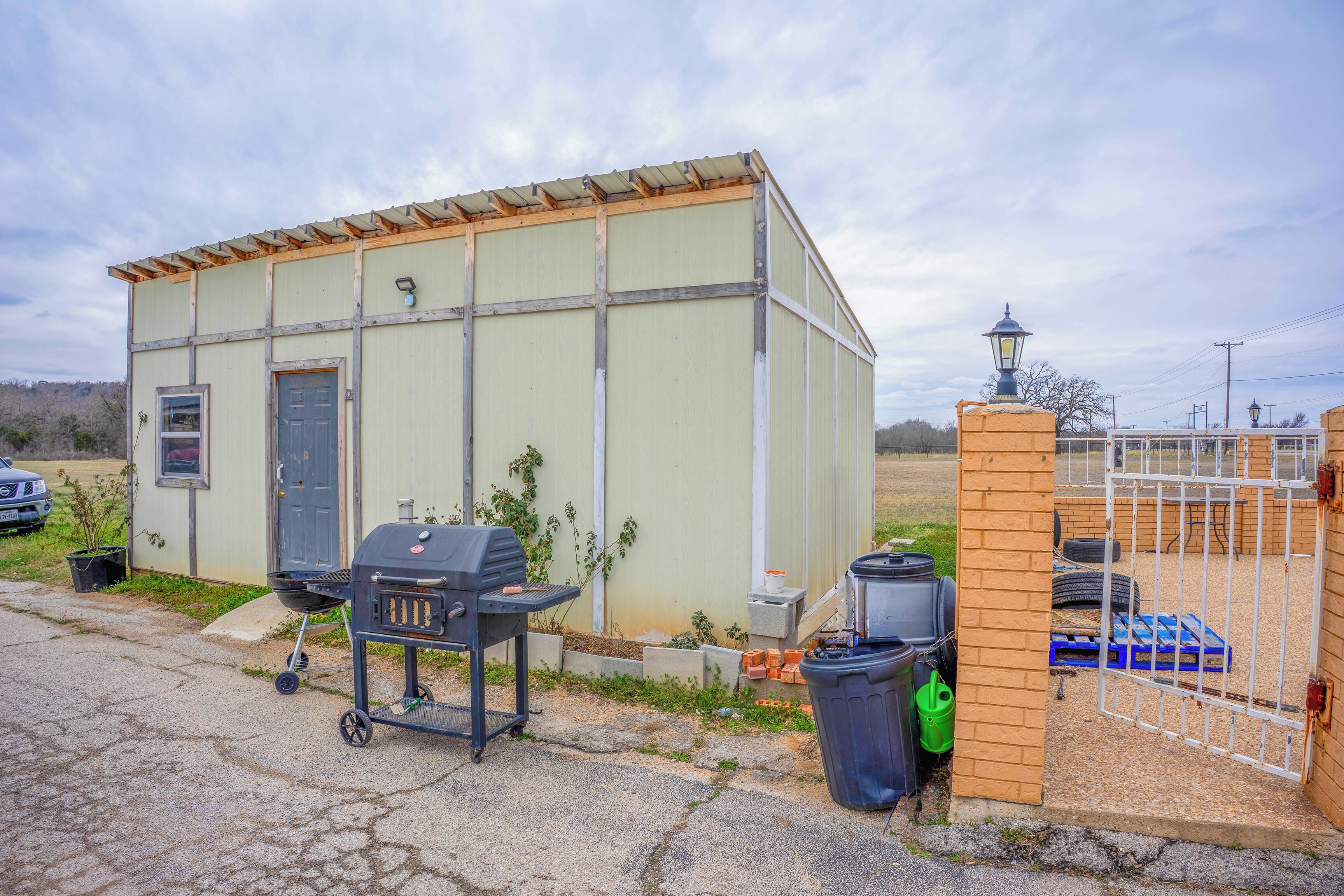 A small, single-story building with a door and windows, a barbecue grill, and a trash bin.