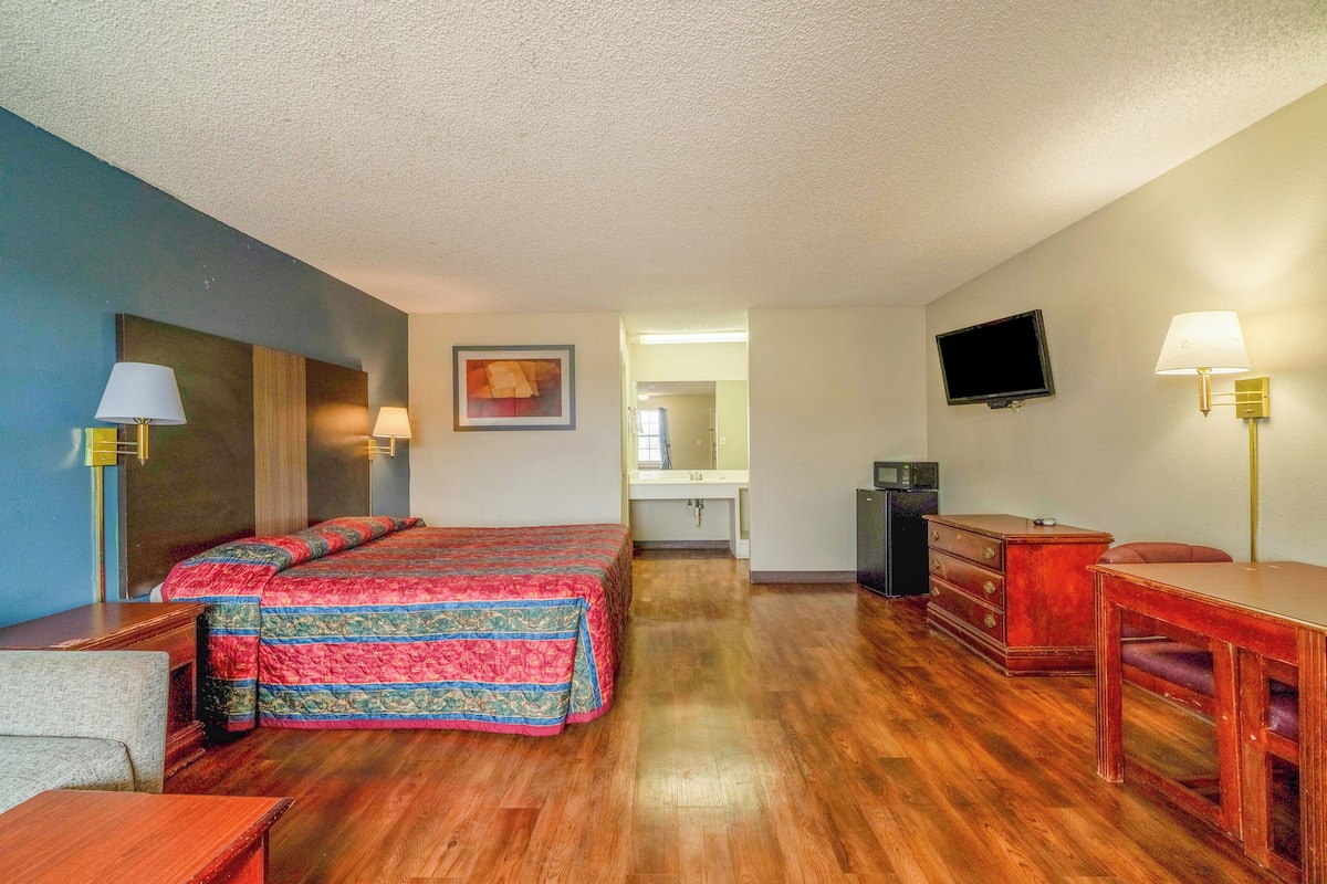 Ein Hotelzimmer mit Bett, Schreibtisch, Stuhl, Fernseher und einem im Hintergrund sichtbaren Badezimmer.