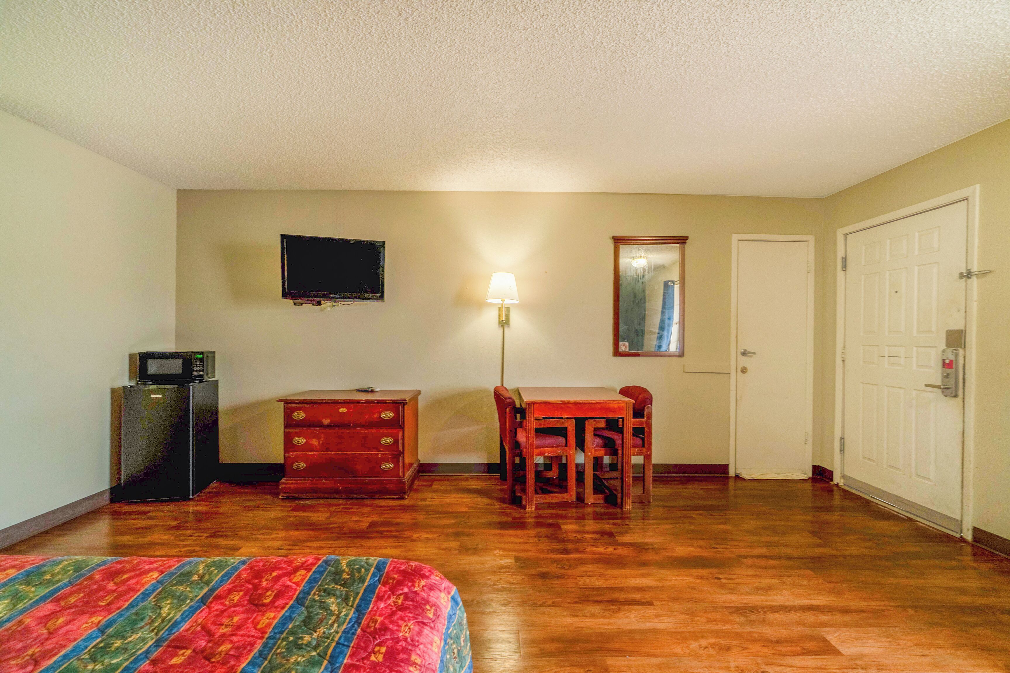 A room with a bed, a desk, a chair, a television, a lamp, a wardrobe, and a door.