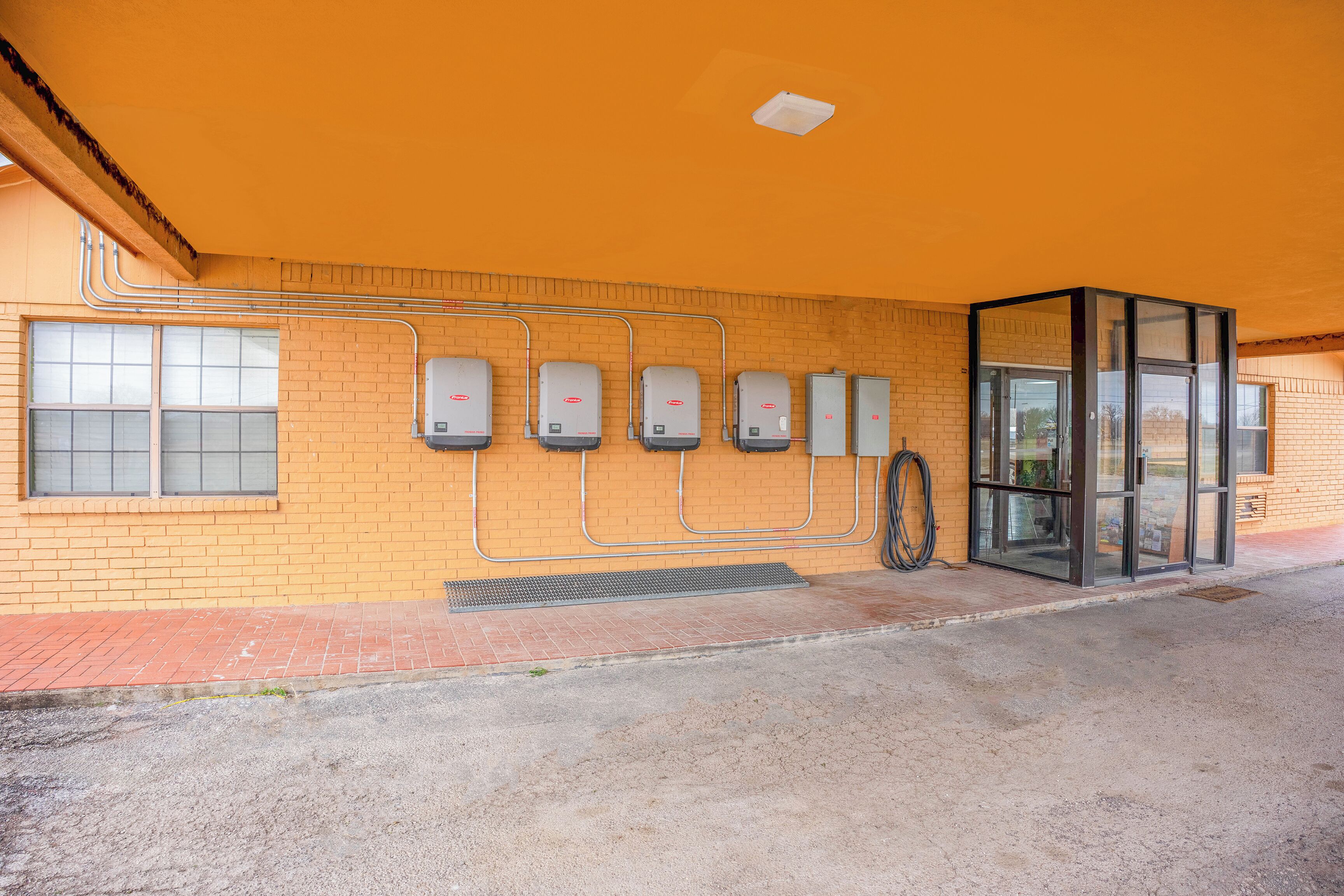 A building with a yellow brick exterior, a glass entrance, and five air conditioning units mounted on the wall.