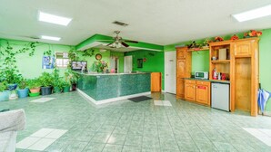 A green-themed reception area with a counter, potted plants, wooden cabinets, and a microwave. - Executive Inn By OYO Mineral Wells US-180 (Mineral Wells)