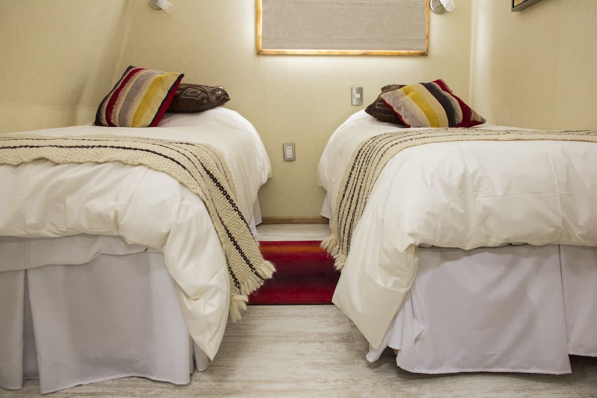 A hotel room with two beds, each with a striped pillow and a white bedspread.