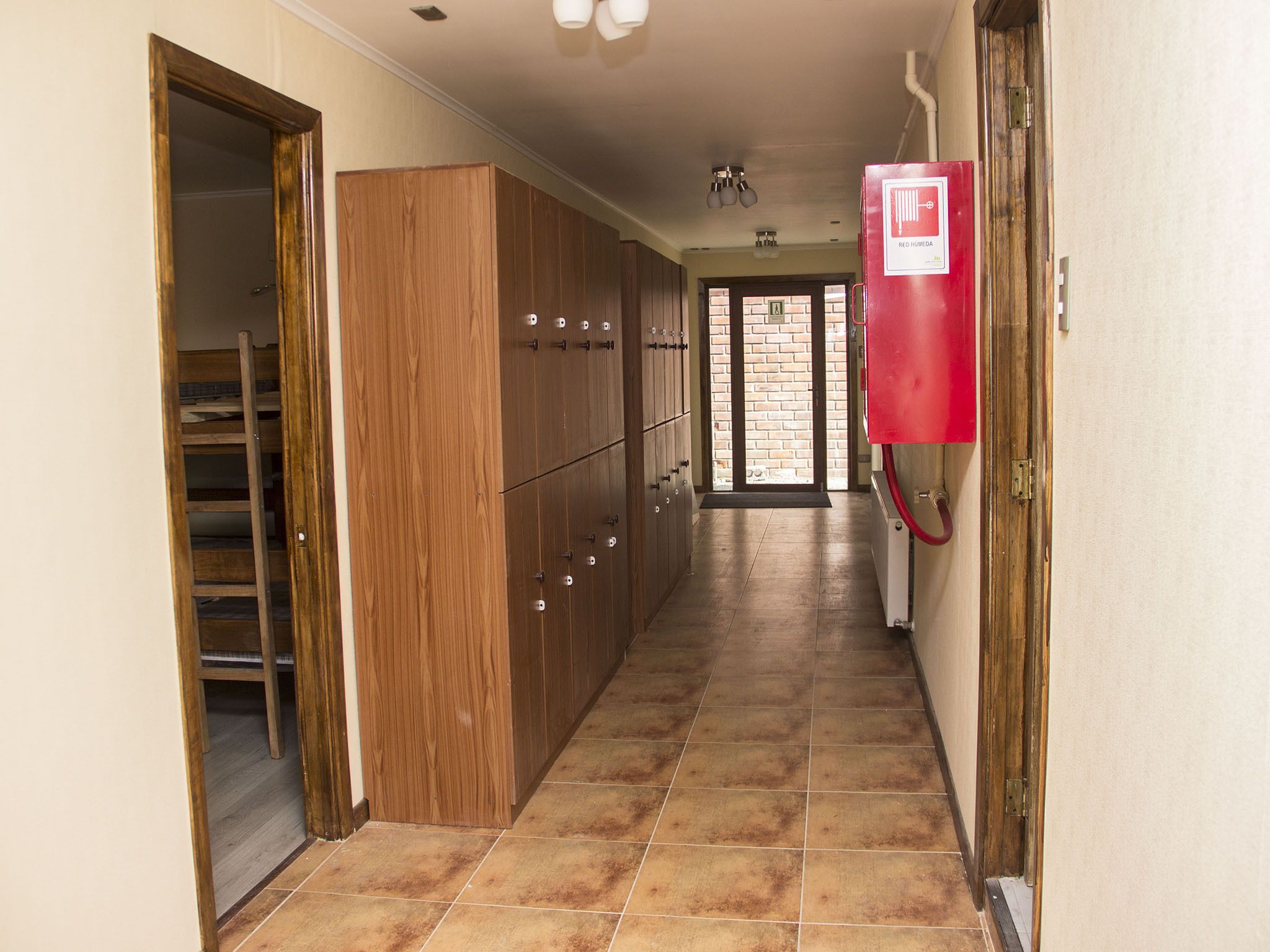 Pasillo con armarios de madera, un detector de incendios rojo y vista al exterior a través de una puerta de cristal.