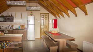 A cozy kitchen with wooden cabinets, a dining table with benches, a red refrigerator, and a foosball table.