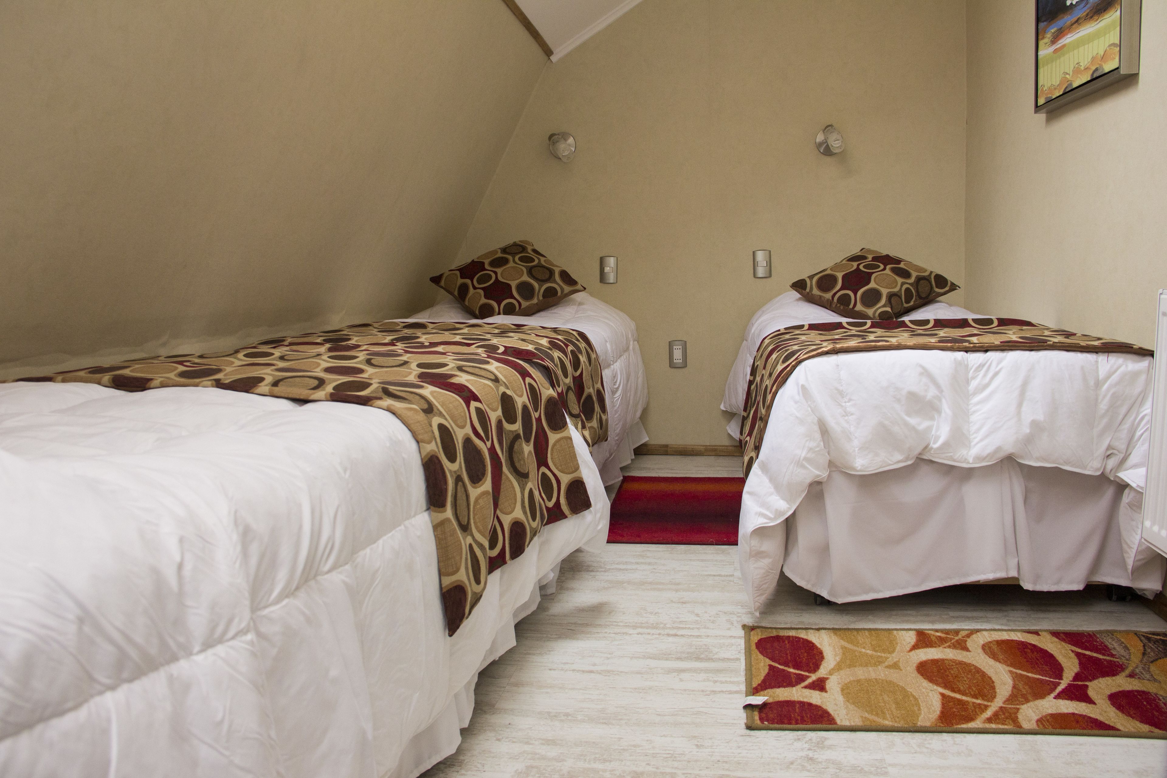 Een hotelkamer met twee eenpersoonsbedden, elk met een beddengoed met een patroon en passende kussens. Er ligt een rood tapijt naar de bedden, en de muren zijn in een neutrale kleur geschilderd.