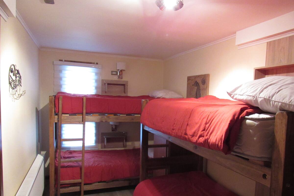 A dormitory room with bunk beds, a radiator, a window with blinds, and a small desk.