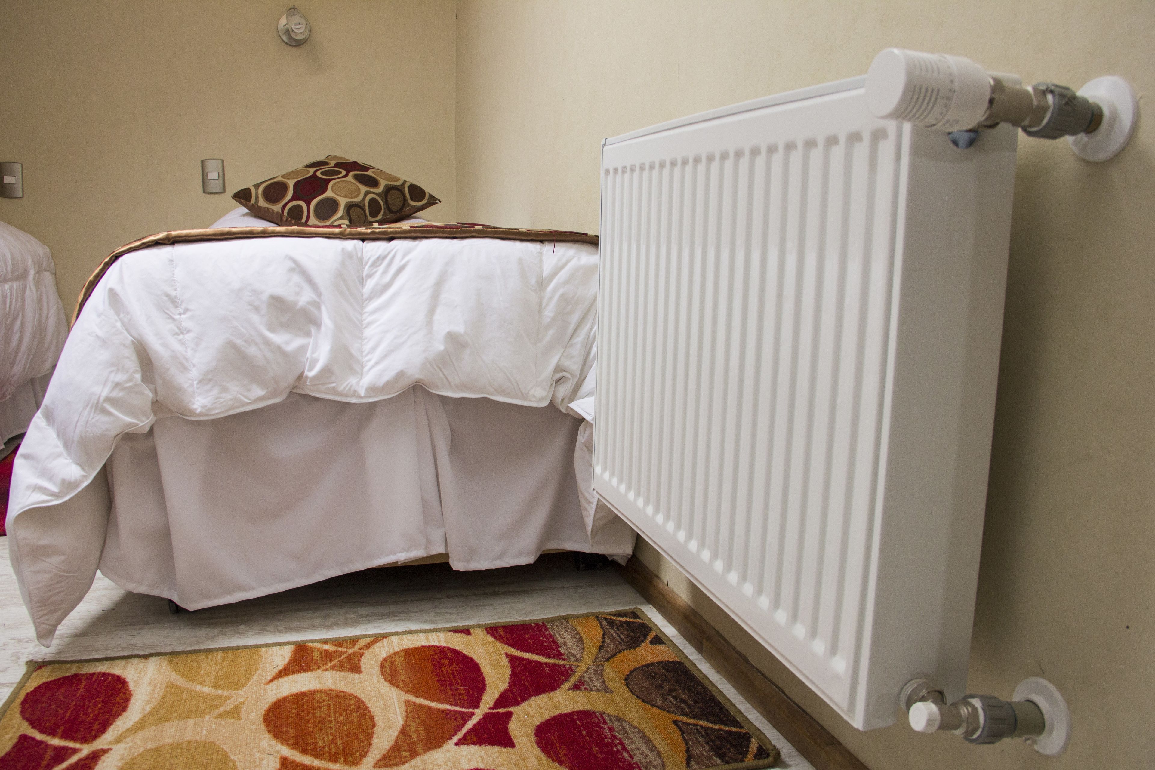 A hotel room with a bed, a radiator, and a patterned rug.